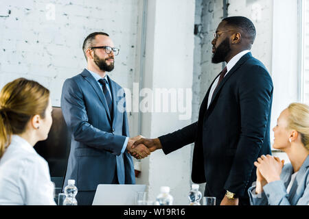 Uomini d'affari multiculturali stringono le mani vicino ai colleghi in ufficio Foto Stock