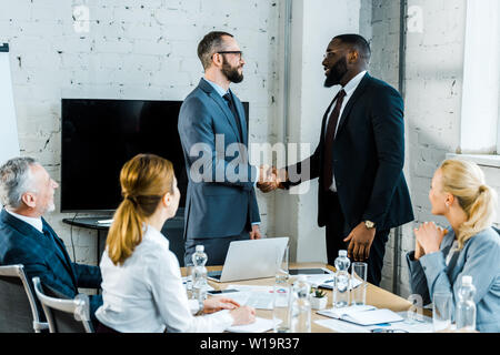 Uomini d'affari multiculturali stringono le mani vicino ai colleghi in sala conferenze Foto Stock