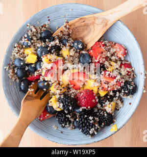 Blue ciotola riempita con insalata di frutta con la quinoa, fette di fragole, pesche noci tritate. more e mirtilli sulla superficie di legno, immagine 7 di 8 Foto Stock