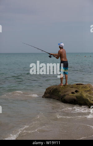 Un giovane uomo pesci off the rocky Oceano Atlantico spiaggia a Carlin Park di Jupiter, Florida, Stati Uniti d'America. Foto Stock