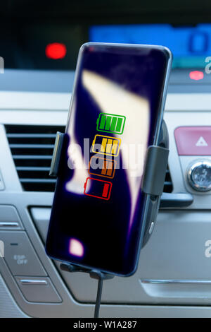 Moderno smartphone wireless in carica in un'auto. Cruscotto in background. Foto Stock