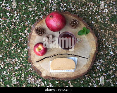 Giugno 2019 - vista superiore di una lastra di Fudge e una tazza di tè su un log decorata con un Apple, melograno, pigne nelle quali e foglie di menta. Foto Stock