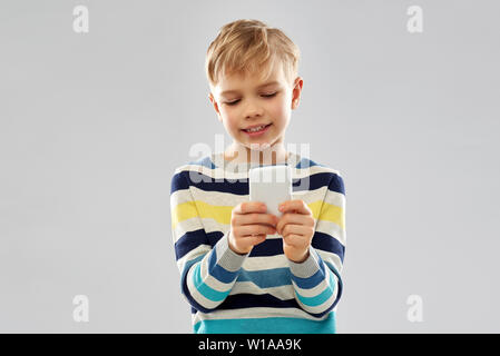 Little Boy in striped pullover utilizza lo smartphone Foto Stock