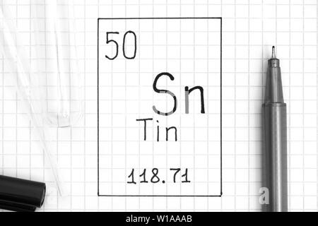 Tavola periodica degli elementi. La grafia elemento chimico Stagno Sn con la penna nera, tubo di prova e la pipetta. Close-up. Foto Stock