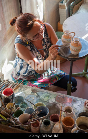 Vernici Craftswoman due piccoli vasi di ceramica nel suo negozio. Diversi pennelli e colori sul suo banco. Foto Stock