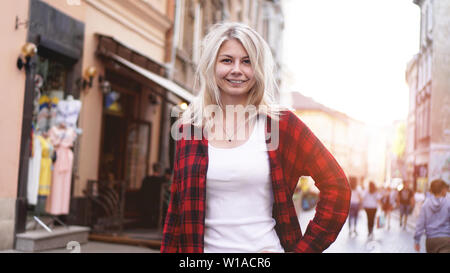 Ritratto di uno stile di vita del quartiere alla moda di felice bionda con capelli disheveled bambina indossa un rock maglietta rossa, bianca t-shirt avendo divertimento all'aperto nella città Foto Stock