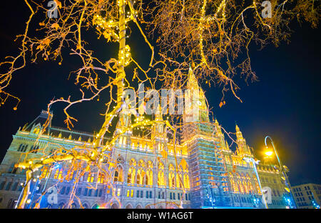 La vista sulla luminosa illuminazione del Rathaus (Municipio) di Vienna tra i rami del parco di alberi, decorata con lampade celebrazione, Vienna, Austria Foto Stock