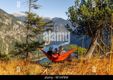 Tre escursionisti seduta in hammocks con vedute delle montagne e del lago, il lago Plansee, Ammergauer Alpi, distretto di Reutte, Tirolo, Austria Foto Stock