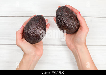 Guardando verso il basso per donna mani due mature brow avocadi su lavagne bianche desk. Foto Stock