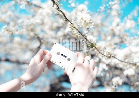 Cassetta nella mani della ragazza sullo sfondo di fiori ciliegio. vintage umore Foto Stock