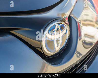 Varna, Bulgaria, 10 febbraio 2019. Chrome blue logo Toyota segno di close-up. La parte anteriore del cofano del blu Toyota auto in un parcheggio all'aperto in una giornata di sole. Foto Stock