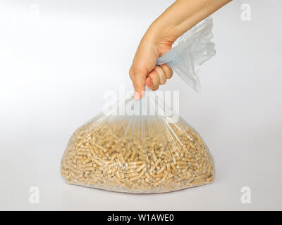 Donna mano trattiene una plastica sacchetto di cellophane con pellet di legno su sfondo bianco. Biocarburanti alternativi da segatura per la combustione nei forni e fornelli Foto Stock