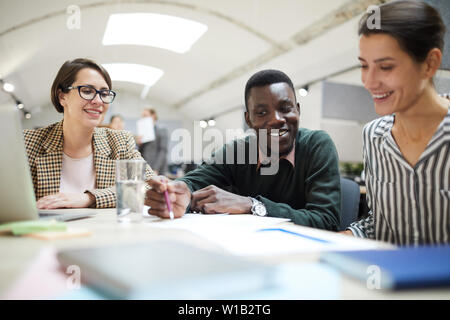 Multi-etnico gruppo di persone sorridenti felicemente mentre lavorando insieme alla scrivania in ufficio, spazio di copia Foto Stock