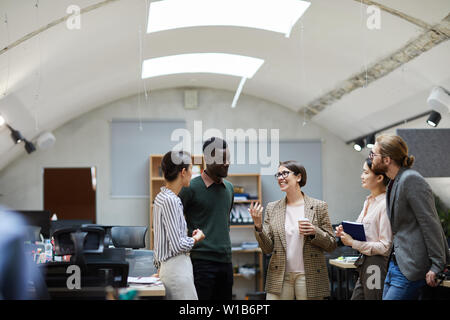 Multi-etnico gruppo di gente di affari di parlare durante la pausa caffè in ufficio sorridendo allegramente mentre, spazio di copia Foto Stock