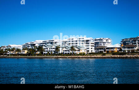 Waterside grandi case costruite nella parte anteriore del condominio con appartamenti Riverside erba, la facciata di pietra della parete di ritegno e il fiume azzurro contro blu chiaro Foto Stock