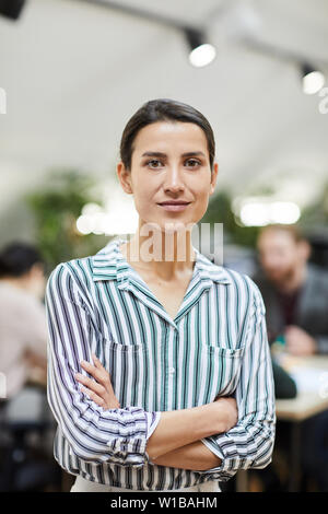 Vita ritratto di Imprenditrice di successo guardando la fotocamera mentre in posa di office in piedi con le braccia incrociate Foto Stock