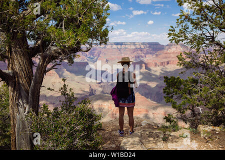 Tourist donna con cappello e zainetto di scattare una foto con un telefono cellulare vicino a una scogliera in South Rim, il Parco Nazionale del Grand Canyon, Arizona, Stati Uniti d'America Foto Stock