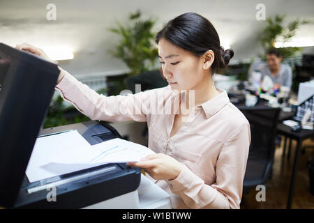 Ritratto di Asian imprenditrice di scansione di documenti mentre si lavora in ufficio, spazio di copia Foto Stock