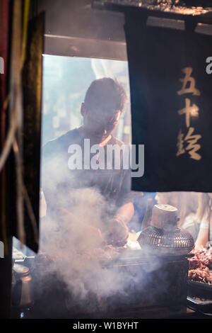 Lavoratore del ristorante prepara il cibo per il cliente al bar tradizionale in Omoide Yokocho, Shinjuku. Orientamento verticale. Foto Stock