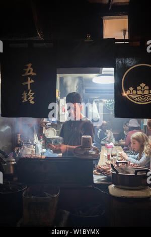 Lavoratore del ristorante prepara il cibo per il cliente al bar tradizionale in Omoide Yokocho, Shinjuku. Orientamento verticale. Foto Stock