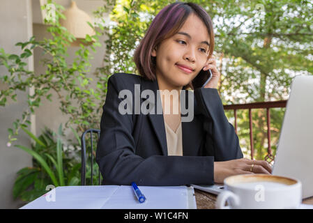 Giovane donna in abito nero utilizzando il telefono cellulare e il computer portatile Foto Stock