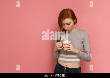 I Capelli rossi ragazza trattiene e cercando nel bicchiere Foto Stock