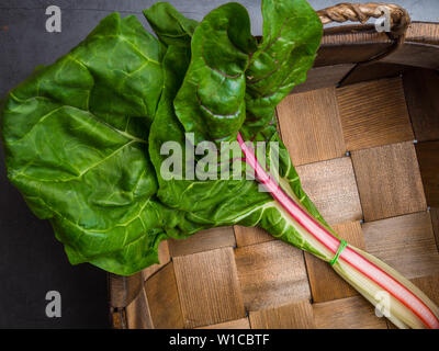 Bietole novelle mangold foglie di insalata nel vecchio cesto sfondo. Vista dall'alto. Mangiare sano tema, alimenti ricchi in cellulosa Foto Stock