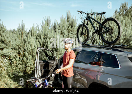 L'uomo la preparazione per le passeggiate in bicicletta, prelievo di bicicletta di montagna dal baule auto durante il periodo estivo nella foresta Foto Stock