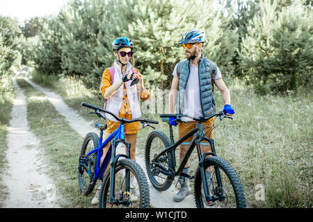 Coppia giovane vestito casualmente a parlare insieme mentre si è in viaggio con la bici di montagna su strada forestale Foto Stock