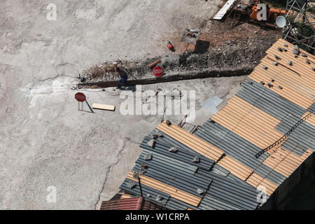 Uomo al lavoro. Lavoratore scava manualmente il fosso lungo nel terreno urbano Foto Stock