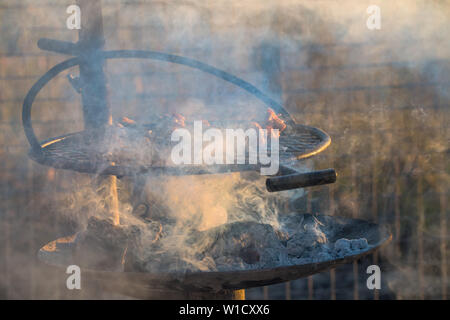 Spiedini di pollo o kebab grigliare su carboni caldi o braci su una griglia di barbecue all'aperto nel bush Africano al tramonto con fumo di vorticazione intorno ad esso Foto Stock