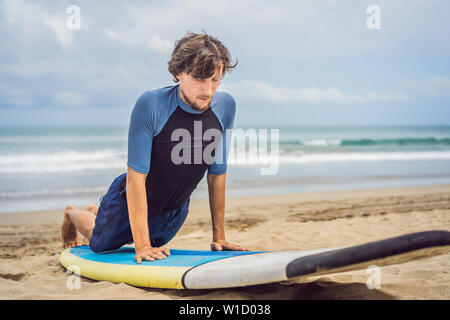 L uomo del surfista sulla spiaggia in fase di riscaldamento prima di Surf, Surf uomo in una muta umida con una tavola da surf sull'oceano, Foto Stock