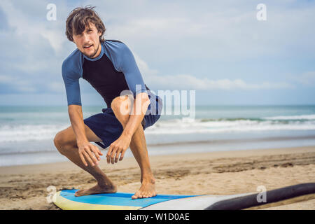 L uomo del surfista sulla spiaggia in fase di riscaldamento prima di Surf, Surf uomo in una muta umida con una tavola da surf sull'oceano, Foto Stock