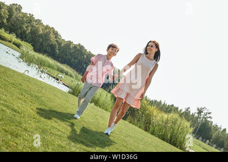 Perfetto figlio. Per tutta la lunghezza della giovane e felice bella madre e figlio per mano e sorridere mentre passeggiate nel parco insieme. Amore e il concetto di famiglia Foto Stock