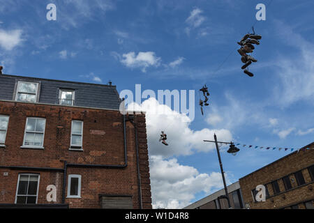 Shoefiti, espressione artistica di imbracatura scarpe legati insieme mediante i loro lacci su linee di alimentazione, nel mercato della cappella, London, Regno Unito Foto Stock
