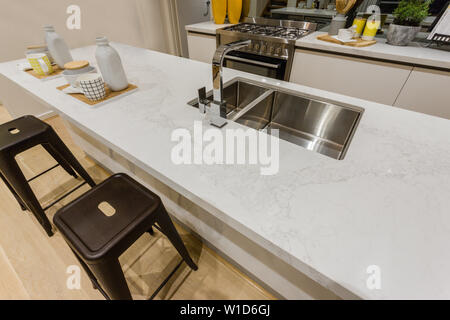 Vista della zona cucina con cucina isola con un stile moderno lavabo, un set di tazza di ceramica e due sgabelli alti. Foto Stock