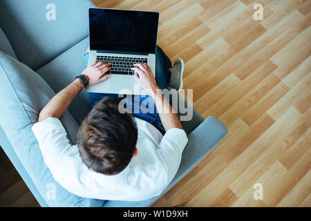 Foto aerea dell'uomo utilizzando laptop rilassante seduta sul divano. Foto Stock