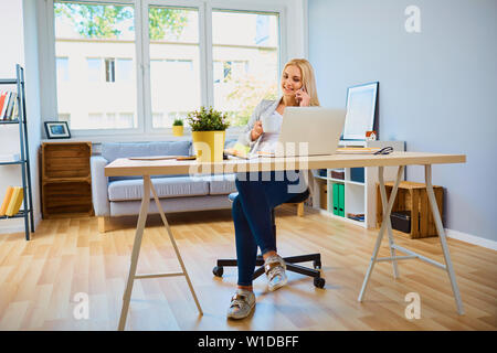 Giovane imprenditrice fare telefonate mentre è seduto in home office Foto Stock