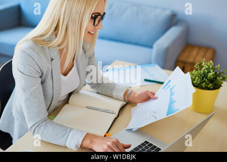 Felice giovane donna che lavorano con i dati finanziari da home office. Imprenditore femmina che lavora da casa Foto Stock