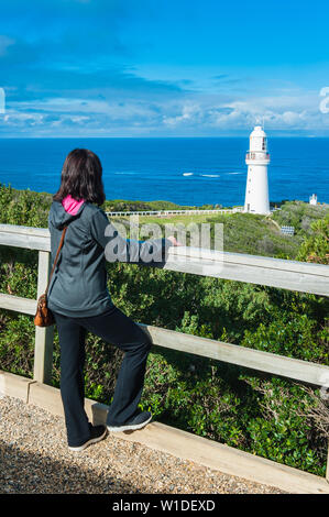 Vista del Faro di Cape Otway a Victoria, Australia come turista femminile gode della spettacolare scena dell'Oceano Meridionale dietro le rotaie di guardia Foto Stock