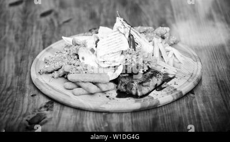 Pub menu snack. Ad alto contenuto calorico snack per il gruppo amici. Gustosi spuntini deliziosi. Il cibo del ristorante. Snack per la birra. Tavola di legno con un sacco di patatine fritte bastoncini di pesce burrito e bistecca di carne con insalata mista. Foto Stock