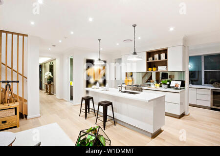 Una elegante scala in legno nella parte anteriore di un elegante cucina componibile con contatori bianchi e cabina e uno snack counter con due sgabelli Foto Stock