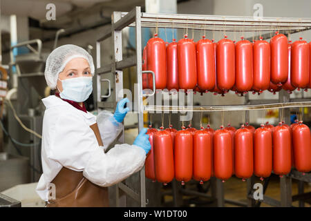 Lavoratore di sesso femminile che trasportano materie salsicce in rack in stanza di deposito alla trasformazione della carne factory Foto Stock