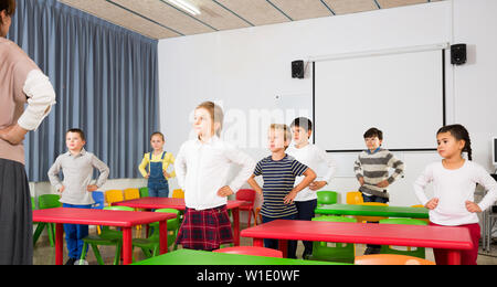 Ritratto di bambini lo stiro con gentile maestro femmina durante l'attività fisica break nella scuola Foto Stock