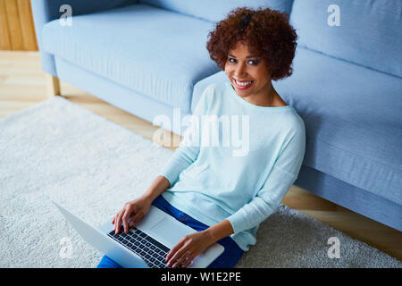 Felice giovane donna africana con laptop seduto in salotto immagine da sopra Foto Stock