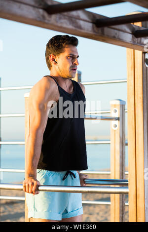 Uomo Forte facendo barra parallela a cali di musica sul terreno di sport sulla spiaggia Foto Stock
