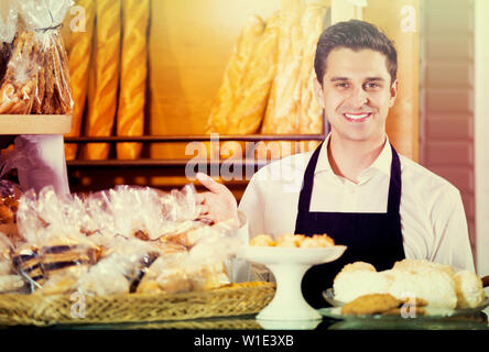 Baker la vendita di pasticceria fresca e baguette nella panetteria locale Foto Stock