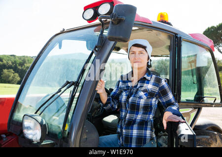 Età della donna positivo lavorando su piccola fattoria trattore Foto Stock