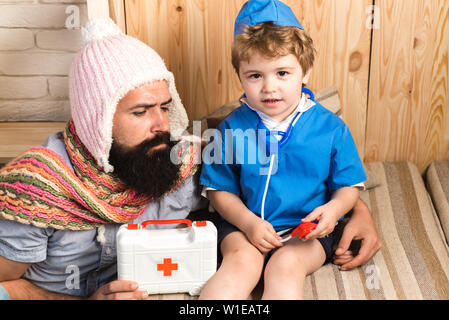 Padre e figlio riproduzione medico a casa. Papà e kid vestito come infermiere. Medicina e salute. Medico con gravi faccia dando istruzioni al barbuto m Foto Stock