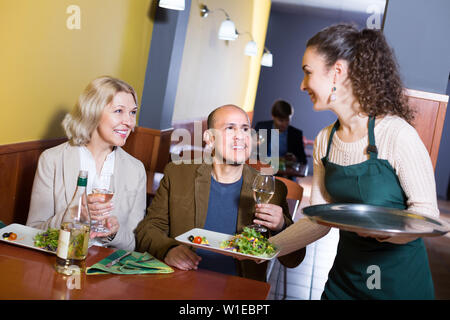 Gentile sorridente cameriera serve coppia di anziani a cena a cafe Foto Stock